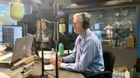Gov. Charlie Baker, wearing headphones, sits in front of a microphone.