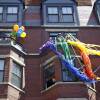 People celebrate from the balconies of brick apartment buildings that are decorated with rainbow streamers and balloons.