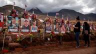 Two people look at portraits posted on a brown grassy hillside, with leis, flowers and flags decorating each.