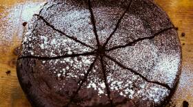 Round chocolate cake dusted with powdered sugar and sliced into wedges