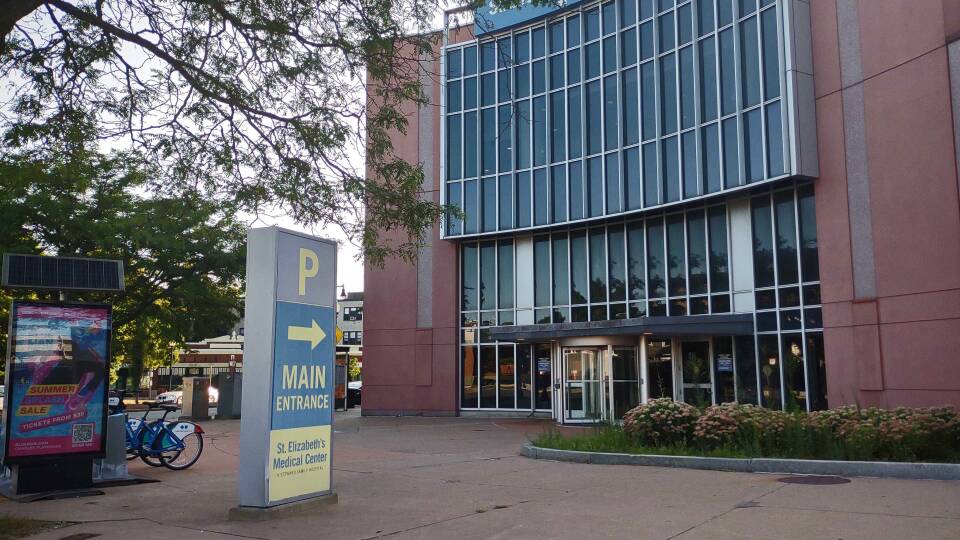 A sign that says "main entrance St. Elizabeth's Medical Center" points toward a rotating glass door on one side of a large building.