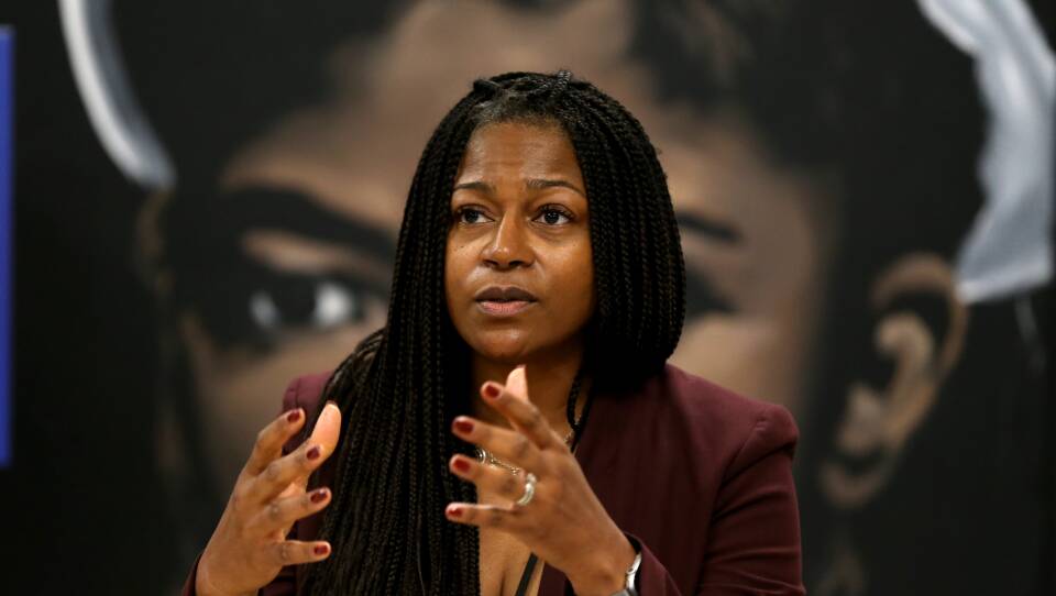 A woman sits, gesturing emphatically with her hands in front of her.