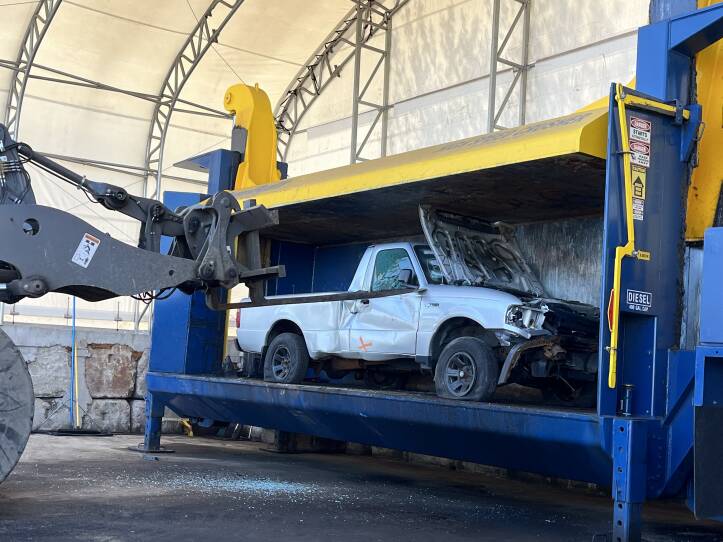 A white truck is severely damaged by dents, flat tires and broken glass as it rests in a large, metal container.