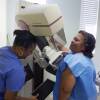 A woman stands at a mammogram machine in a hospital during a routine screening.