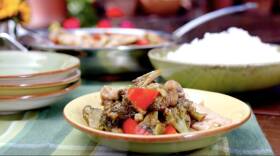 Bowl on a green plaid placemat filled with lightly sauced pieces of chicken, red peppers, mushrooms, and broccoli