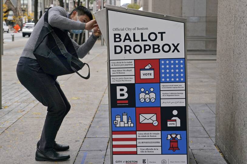 A person squats down to peer inside the slot of a ballot drop box as they put their ballot inside.