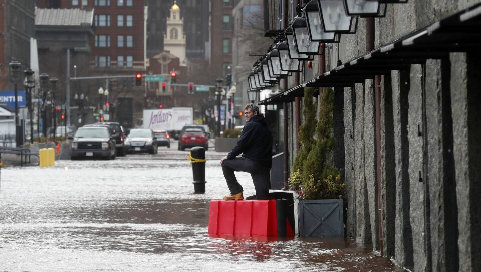 A man stands in the street as flooding up to the ankles or knees laps on a Boston street.