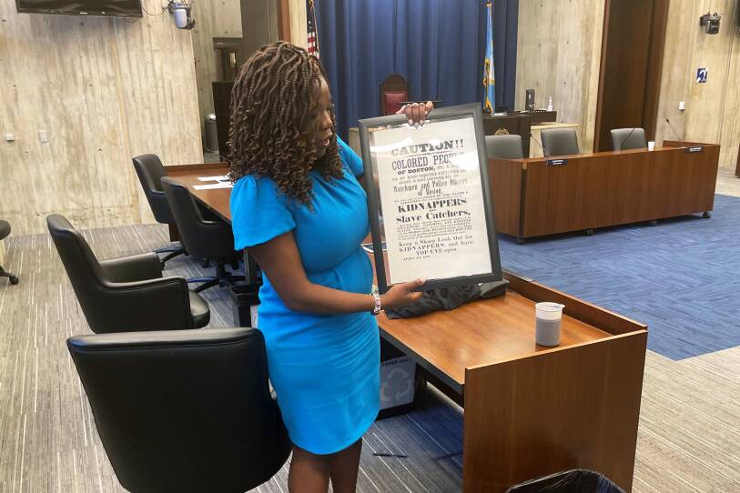 Boston City Councilor Ruthzee Louijeune holds a framed reprint of a poster that warned freed Blacks in Boston of local enforcement of the federal Fugitive Slave Act.