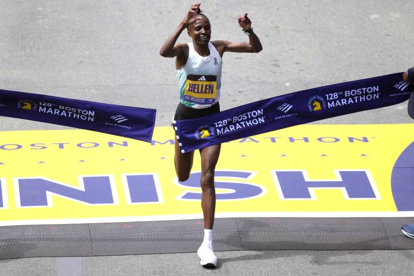 An elite runner raises her hands in joy as she breaks through the finish line at the Boston Marathon.
