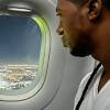 A man with a few hanging dreadlocks looks out the window of a plane.