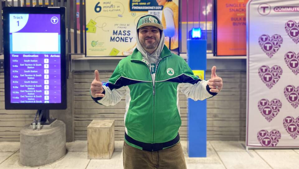 A man wearing a Celtics shirt holds two thumbs up.