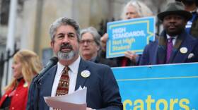 A man in a suit and tie speaks into a microphone at a rally.