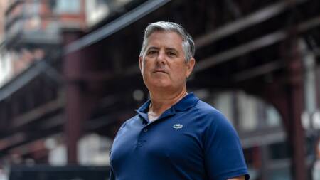 A man in a blue polo shirt stands on the sidewalk underneath Chicago's L train tracks.