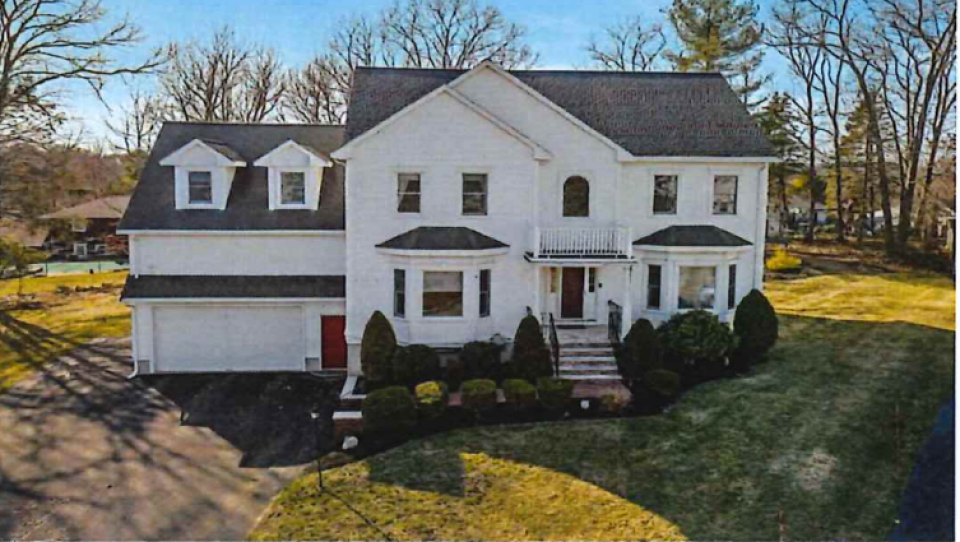 A white two-story single-family house sits in a grassy yard with trees at the edges.