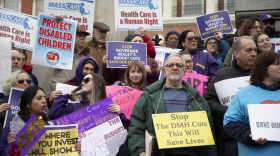 Dozens of people rally with signs advocating against Department of Mental Health cuts.