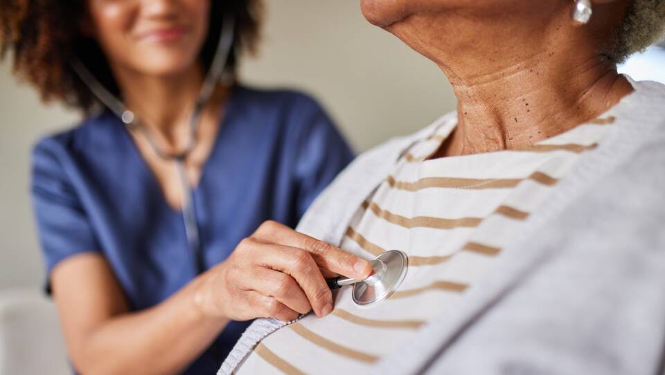 A doctor listens to an older woman's heart with a stethoscope.