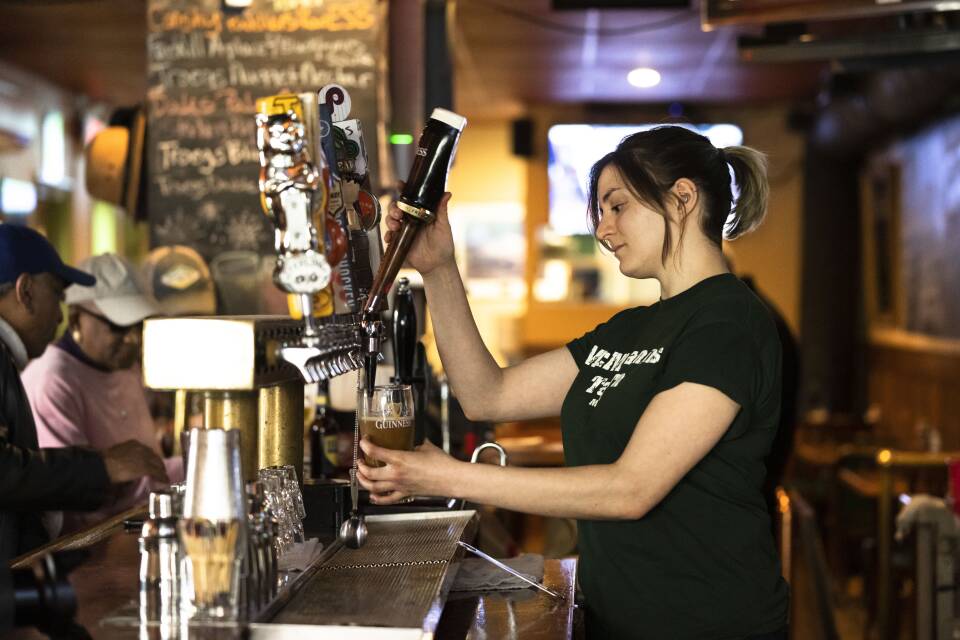 A woman pulls a draught beer from behind the bar.