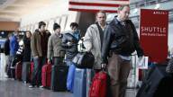A line of people in an airport with their bags.