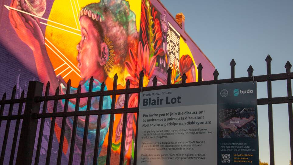 A sign posted to a fence around the Blair Lot invites community members to join the discussion. A mural with a Black child and flowers is behind the fence.