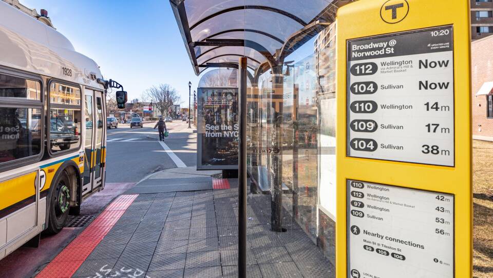 An electronic sign shows bus arrival times for several different lines next to a shelter.