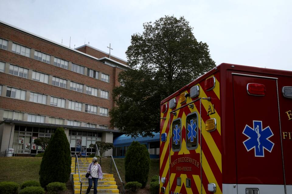 A woman walks out of a hospital that has an ambulance parked outside.