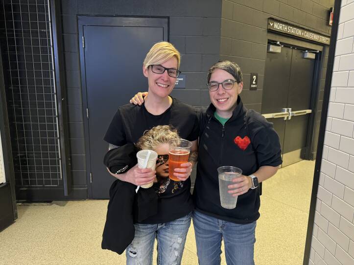 Two women stand with their arms around each other, wearing Madonna shirts. They are holding drinks in their hands.
