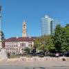 A person walks past a park containing a tall statue and large building. A sign along the sidewalk reads "Worcester Common"