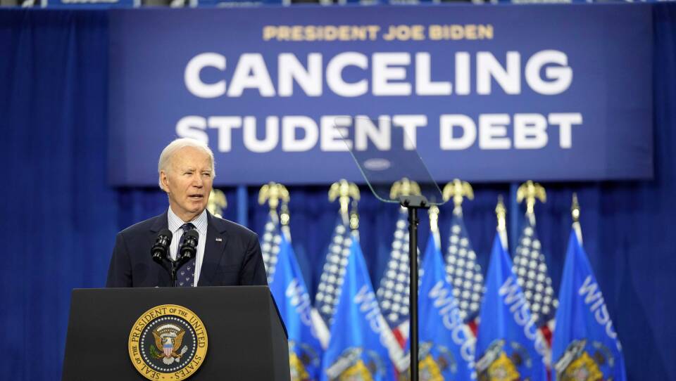 Joe Biden speaks at a podium. Behind him are a row of flags and a sign that says "canceling student debt"