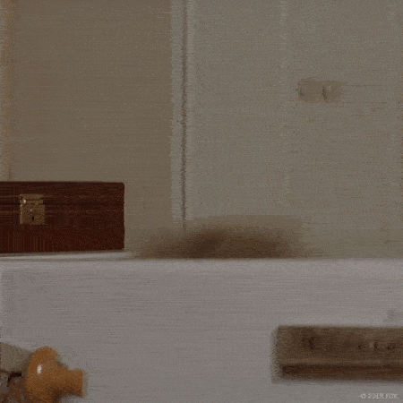 A man dressed as an elderly woman pops up from behind a fridge, face covered in frosting, and says "hello!"