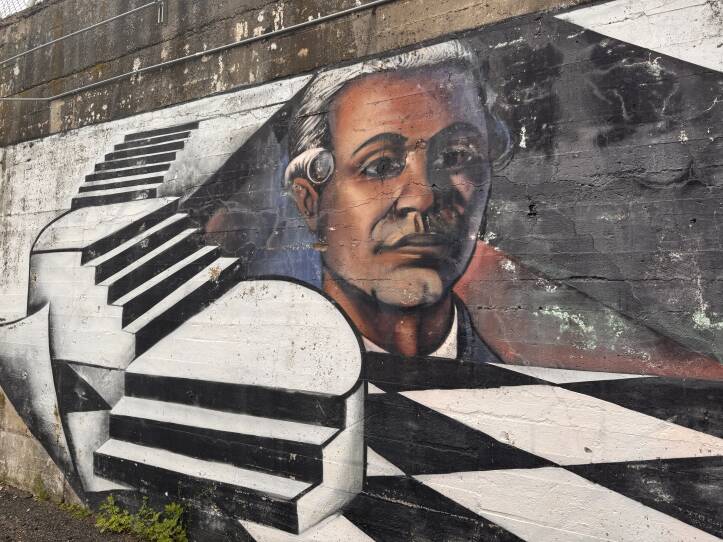 A mural on a concrete wall of a Black man from the colonial era with a powdered wig and white steps.