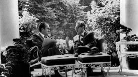 Two men sit on an outdoor patio facing one another. deep in conversation. Black and white image.