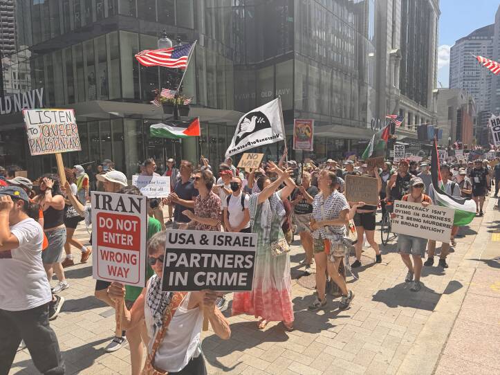 Dozens of people holding signs opposing U.S. airstrikes on Iran march down a street in Boston.