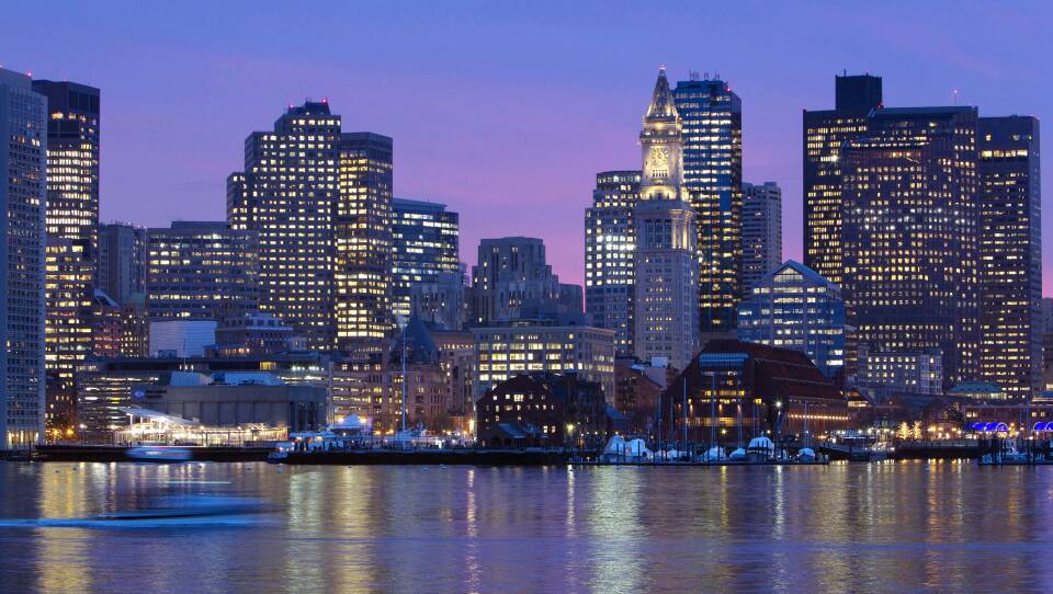 A purple and pink sky lingers over downtown Boston as lights in buildings turn on for the night.