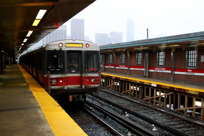 A subway train sits on the tracks at an above-ground station on a cloudy day.