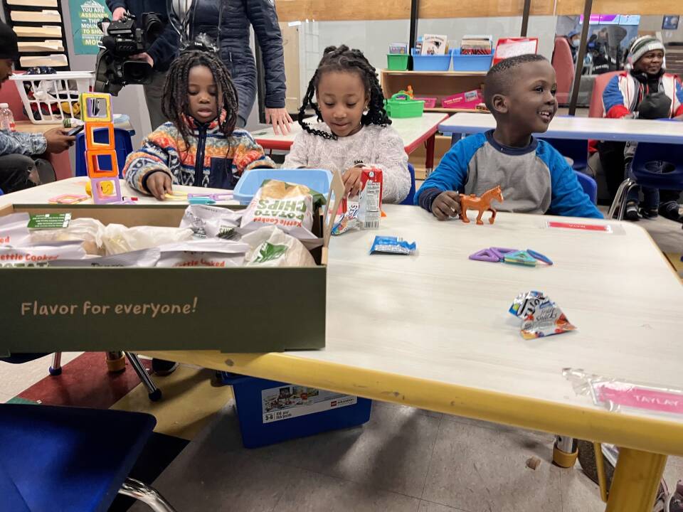 Three young Black kids sit at a table, playing with toys.