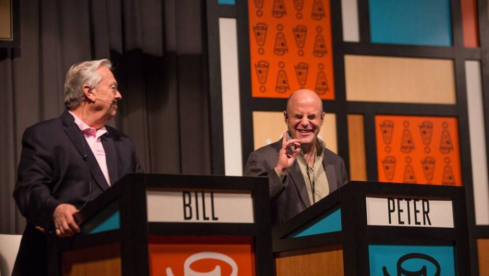 Two men on a game show set, with the names Bill and Peter written on their respective podiums.