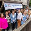 A group of people, including Governor Healey, poses and smile standing outside a clinic. A sign above them says 'Health Imperatives.'