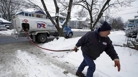 On a snowy day, a worker pulls a hose from a tanker truck with heating oil.