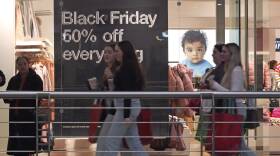 Five people walk past a clothing store in a mall.