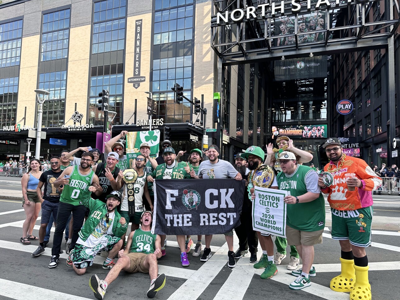 A group of people all wearing Celtics gear holding up signs stand and pose outside the TD Garden.