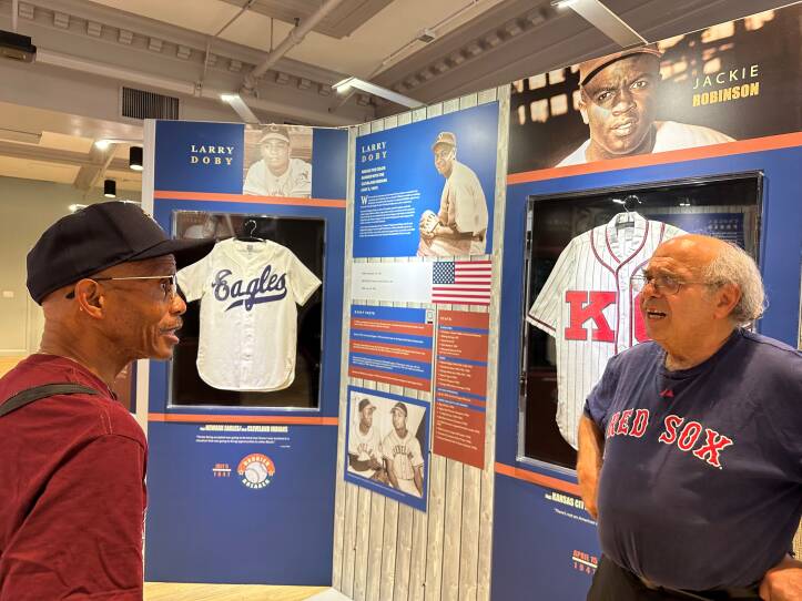 Two men speak at each other in front of displays on Larry Doby and Jackie Robinson.