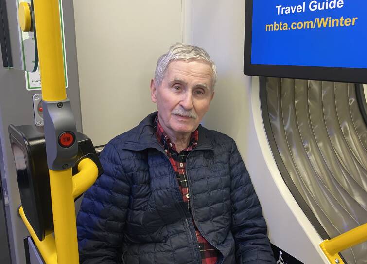 A man wearing a lightweight jacket sits in a single seat near the door of a subway car.