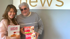 A woman and man pose for a photo with the branded Dumpling Daughter frozen food and cookbook.