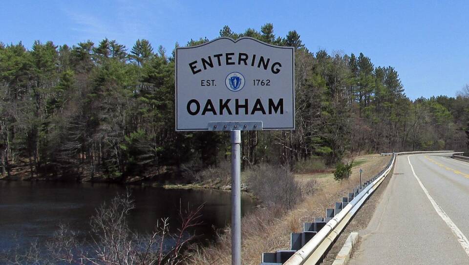 A book-shaped sign posted by the side of a road reads "Entering Oakham, est. 1762"