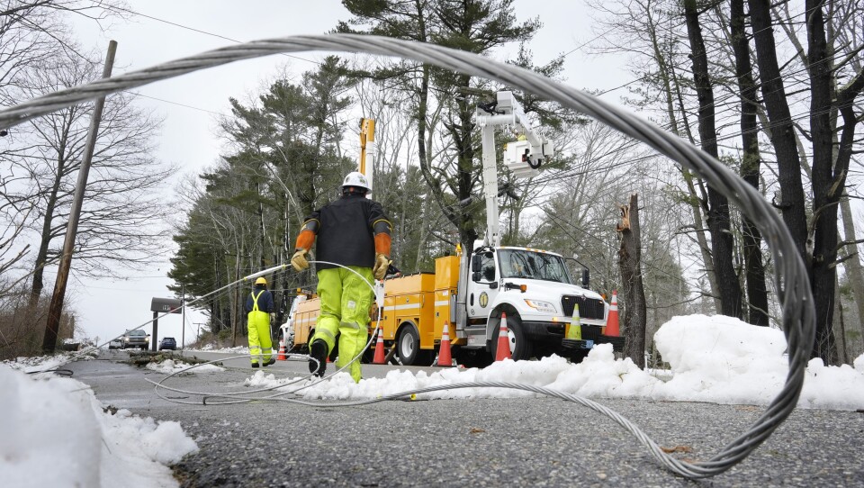 An electrical guardwire sweeps across the frame behind a utility worker walking toward their truck.