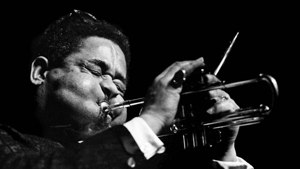 A man with huge, inflated cheeks blows into a horn as he performs on stage.