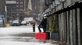 A man stands in the street as flooding up to the ankles or knees laps on a Boston street.