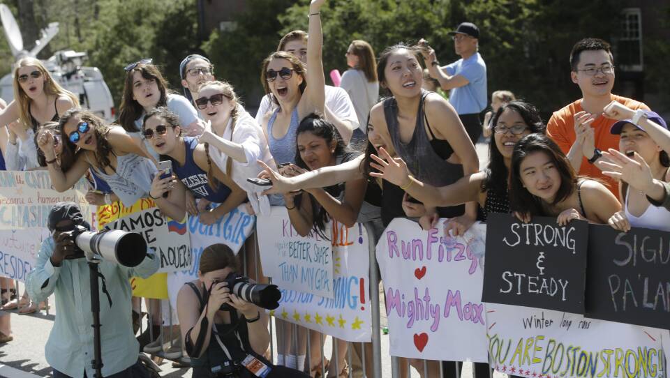 A group of mostly young women cheer excitedly over the rails of barricades with large posters to cheer on runners.