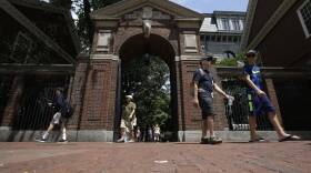 A handful of people who appear to be parents and students walk on the brick sidewalk on the edge of Harvard's campus.