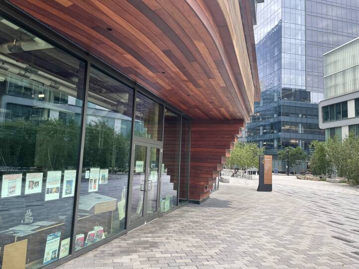 This is an exterior photograph of a bookstore. The photo is taken from the side. There are glass windows with book displays.